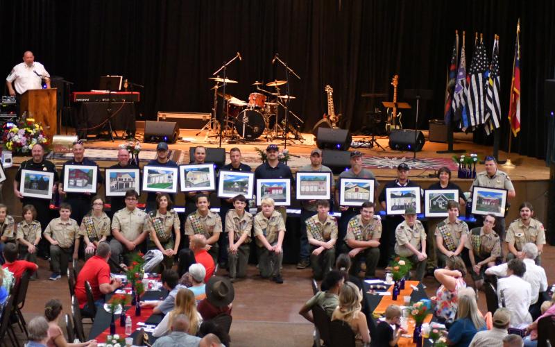 Enoch Autry/The Clayton Tribune. The Boy Scouts presented the first responders with paintings of the structures in the county for law enforcement, EMS and others. Below:  Sheriff Chad Nichols sits with his 6-year-old son Chatham at the banquet.