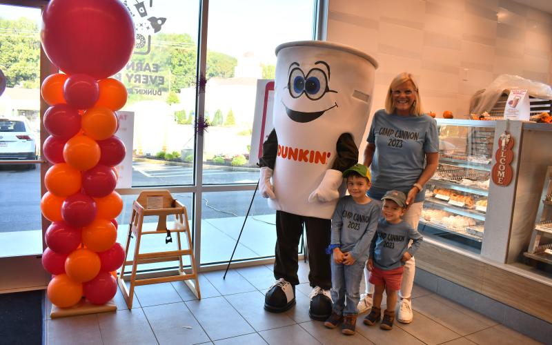 Megan Horn/The Clayton Tribune. Cathy Cannon and grandchildren John Walker Self, 4-and-a-half, and Travis Self, 2-and-a-half, are excited to see Cuppy during the Dunkin' Donuts grand opening event. Below: Megan Horn/The Clayton Tribune. Lucy Woerner poses with Cuppy during the Sept. 30 Dunkin' Donuts grand opening. 