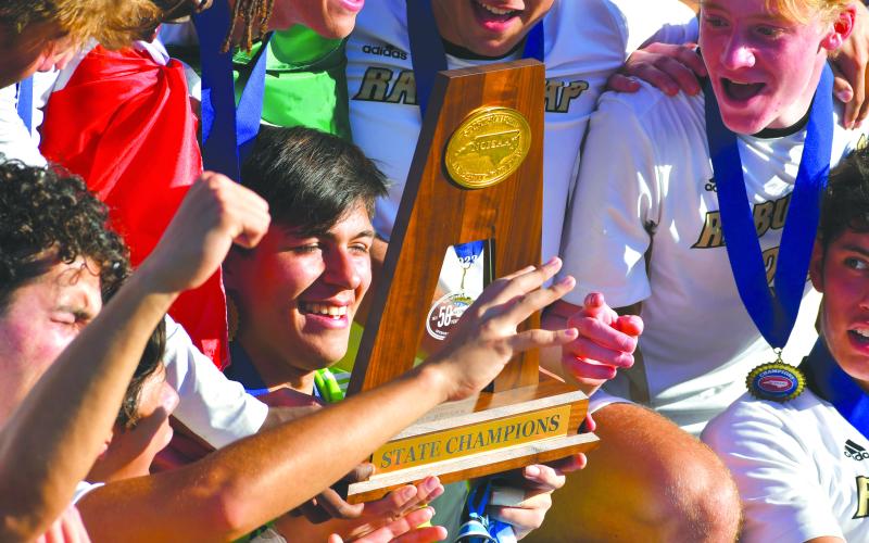 Wade Cheek/The Clayton Tribune. Rabun Gap goalkeeper Agustin Canales smiles as he looks down at the 2023 NCISAA championship trophy after RGNS won the NCISAA state title. The championship was the Eagles’ third straight.