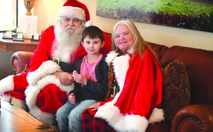 Megan Broome/The Clayton Tribune. Santa and Mrs. Claus took a break from Christmas preparations at the North Pole to visit with children in Rabun County Monday. The cheerful duo was spotted at Better Homes and Gardens Real Estate Metro Brokers in Clayton. The business was decorated with Christmas cheer and Santa and Mrs. Claus passed out cookies and candy canes to children. Pictured is 6-year-old Jace Shirley who is excited to meet Santa and Mrs. Claus. 