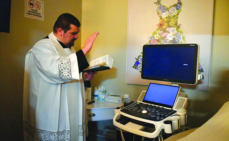Megan Broome/The Clayton Tribune. Father Luis Alvarez blesses the new ultrasound machine. 