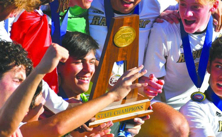 Wade Cheek/The Clayton Tribune. Rabun Gap goalkeeper Agustin Canales smiles as he looks down at the 2023 NCISAA championship trophy after RGNS won the NCISAA state title. The championship was the Eagles’ third straight.