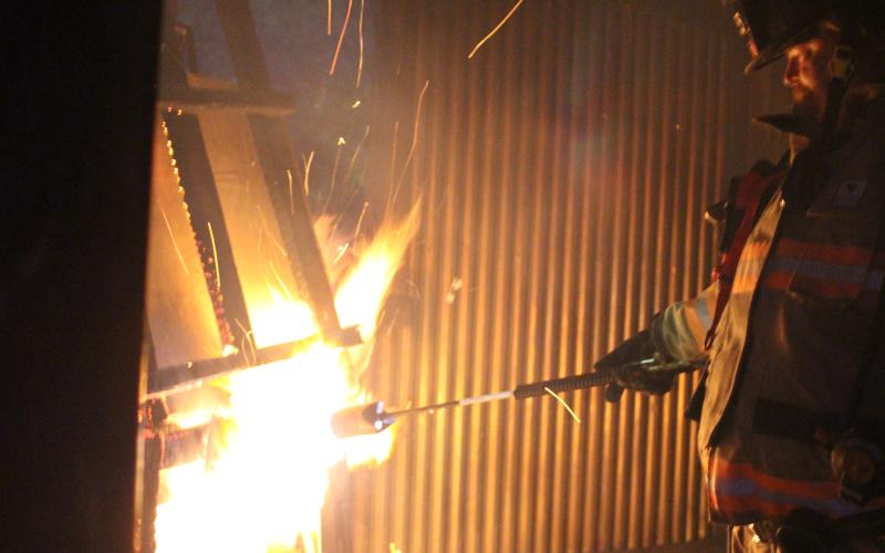 Megan Broome/The Clayton Tribune. Jerry Buice lights a pile of wood on fire inside a metal building used for firefighter training at the Rabun County Fire Services training center at Station 4 in Lakemont.