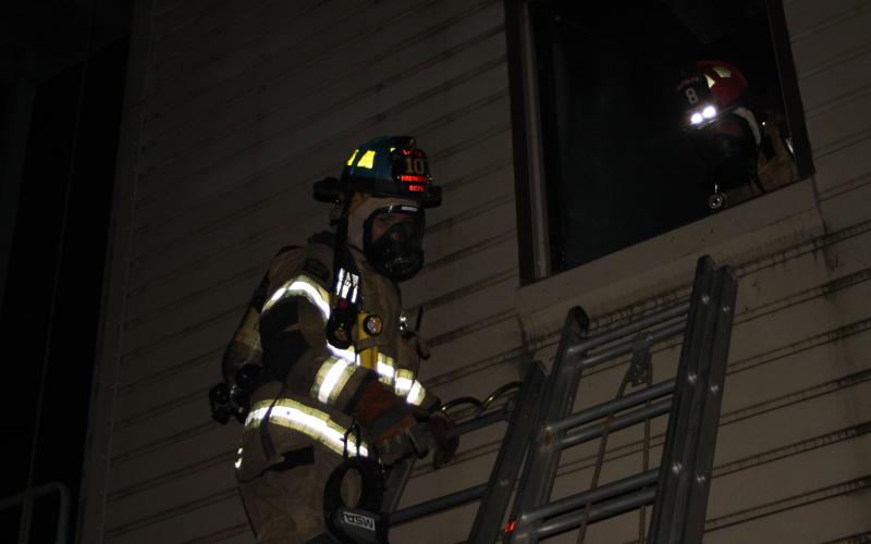 Firefighters ascend a ladder to assist in a training exercise on the second floor of the metal building simulating a structure fire.