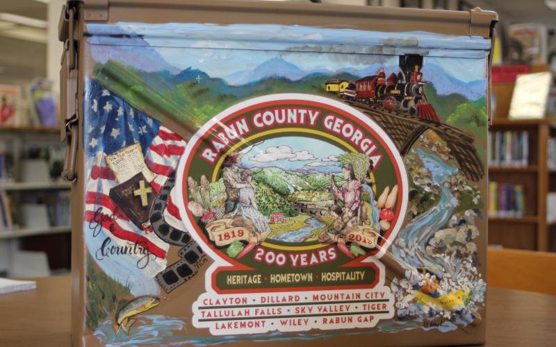 Megan Broome/The Clayton Tribune. The time capsule that will be buried for the Rabun County Bicentennial and opened in 100 years was painted by local artist Diane Rush. The time capsule is a military ammo box that was donated by Alan Price.