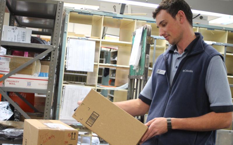 Megan Broome/The Clayton Tribune. Colby Nichols organizes packages for shipment at the Clayton Post Office on Monday. The Post Office saw a 14 percent increase in packages compared to the same time last year.