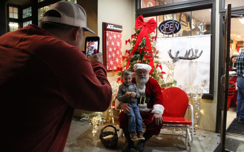 Rawlin Maxwell, 3, pays Santa Clause a visit while his grandfather Darren Dickerson snaps a picture during Christmas in Downtown Clayton