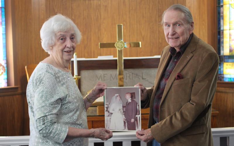 Megan Broome/The Clayton Tribune Catherine Turpen and Rev. James E. Turpen, Sr. stand in front of the altar at Tallulah Falls United Methodist Church and hold a picture from their wedding day where they said “I do” in the same spot  55 years ago on Dec. 20, 1964.