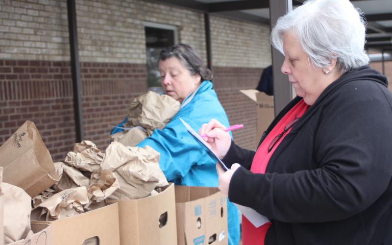 Megan Broome/The Clayton Tribune Elisa Tate, cafeteria worker at Rabun County Schools, left, and Reneta “Skeet” Hollifield, cafeteria manager at Rabun County Primary School (RCPS), pass out sack lunch meals at RCPS on Monday so that students have food to eat while school is closed due to COVID-19 concerns.