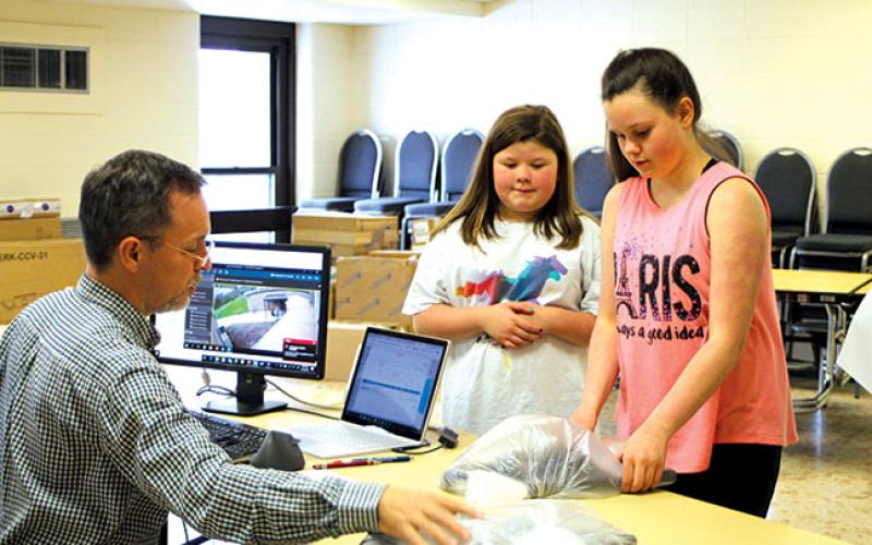 Megan Broome/The Clayton Tribune. Greg Purcell, technology director for Rabun County Schools, hands out Chromebooks to fifth grader Nevaeh Fain and sixth grader Hanby Denning during distribution at the Board of Education Office on Tuesday. The Chromebooks will allow students to complete online learning while students are out of school due to COVID-19.