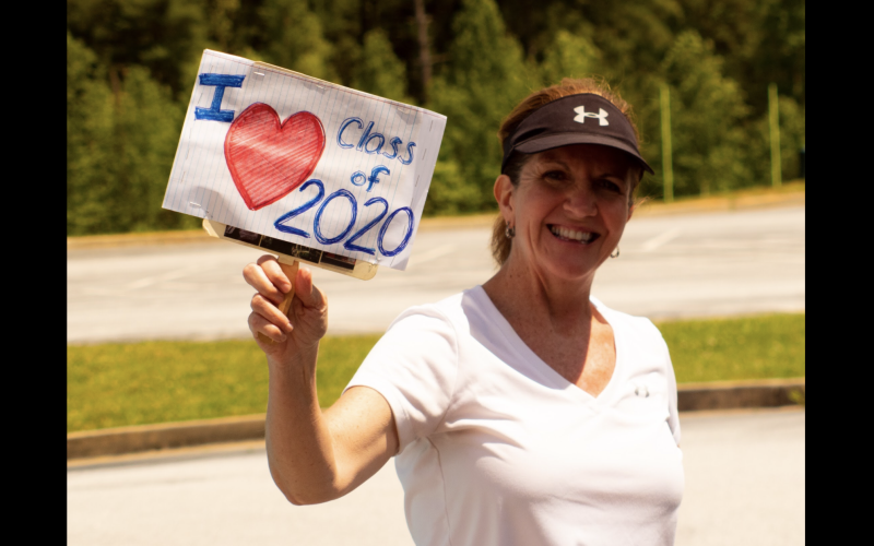 Photo courtesy Rabun County Schools. Jane Johnston, RCHS math teacher, shows her support for the Class of 2020. Rabun County High School seniors picked up their senior packets of their cap, gown, and care package last Friday. Family, friends, school officials and community members show their love to the Class of 2020 by decorating cars, holding up signs and waving and cheering as cars go by.