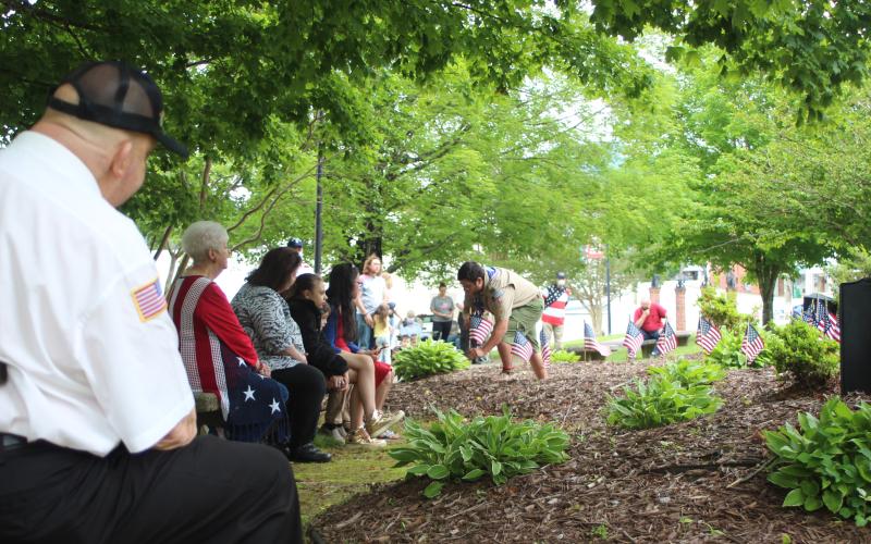 Megan Broome/The Clayton Tribune. Mickey Wood, left, and Francesca Franklin, along with members of the community watch as Dominic Cross places flags at the Veterans’ Monument in front of the Rabun County Courthouse as the names of all those in the armed forces who have passed away in the last year were read aloud.