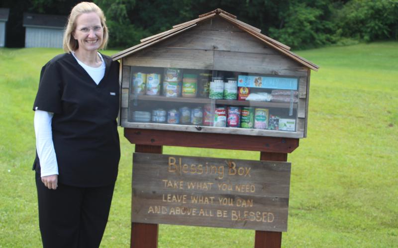 Megan Broome/The Clayton Tribune.Shannon Robinson stands beside the “Blessing Box”  stocked with canned food items and other foods like peanut butter, canned fruit, rice, cereal, beans and other essential items available for free to anyone in need.