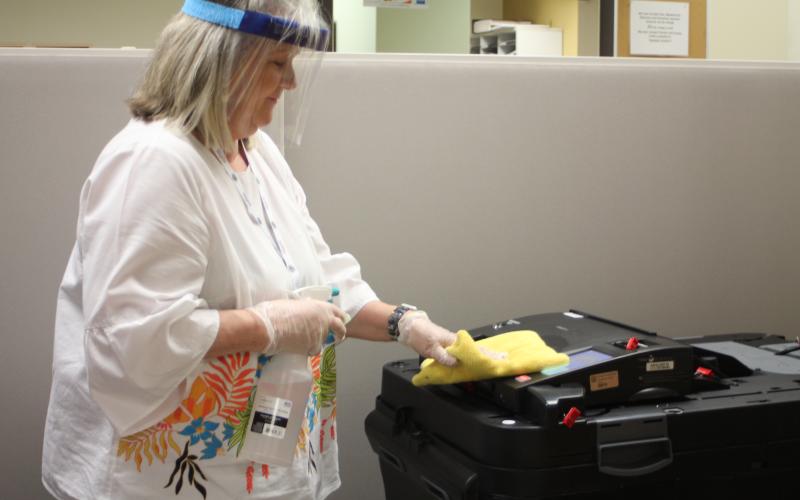 Megan Broome/The Clayton Tribune. Poll Worker Pat Hopper disinfects the entire voting area at the Board of Elections Office after each person finishes casting their ballot. Only one voter at a time is allowed inside the building for early voting as part of COVID-19 contact precautions.
