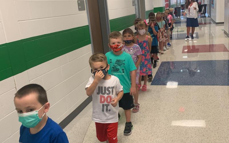 Photo courtesy Rabun County Schools. Jax Jackson, left, Asher Justice, Jordan Whipple and Kasi Jai Blalock from Mrs. Moore’s kindergarten class stand single-file in the hallway wearing masks during the first week of school as part of COVID-19 safety measures in the school system. One-direction hallways are part of the “new normal” for the school year.