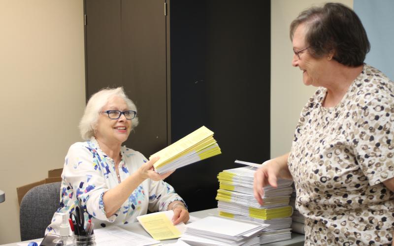 Megan Broome/The Clayton Tribune. Elaine Lawson, absentee ballot clerk for the Rabun County Board of Elections Office, right, hands a stack of completed absentee ballots to poll worker Ann D’Agostino for processing at the Board of Elections Office Tuesday.