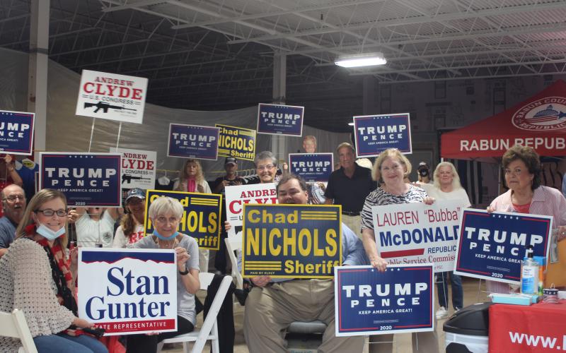 Megan Broome/The Clayton Tribune. Members of the Rabun County Republican Party and community patrons hold up campaign signs at the grand opening of their campaign headquarters last Saturday.