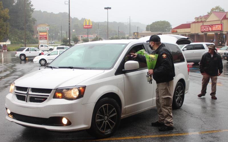 Megan Broome/The Clayton Tribune. Rabun County Detention Center Officer Daniel Nicholson hands out flowers and chocolate to families during the Faith and Blue food distribution event last Saturday. Each family was given these along with boxes of food.