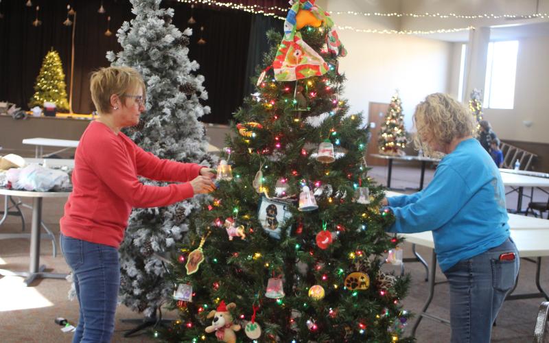 Megan Broome/The Clayton Tribune. Mary Baer, left, and Meg Starzec help decorate a Christmas tree and set up for the Merry Market and Fundraising Jolly happening Friday and Saturday.