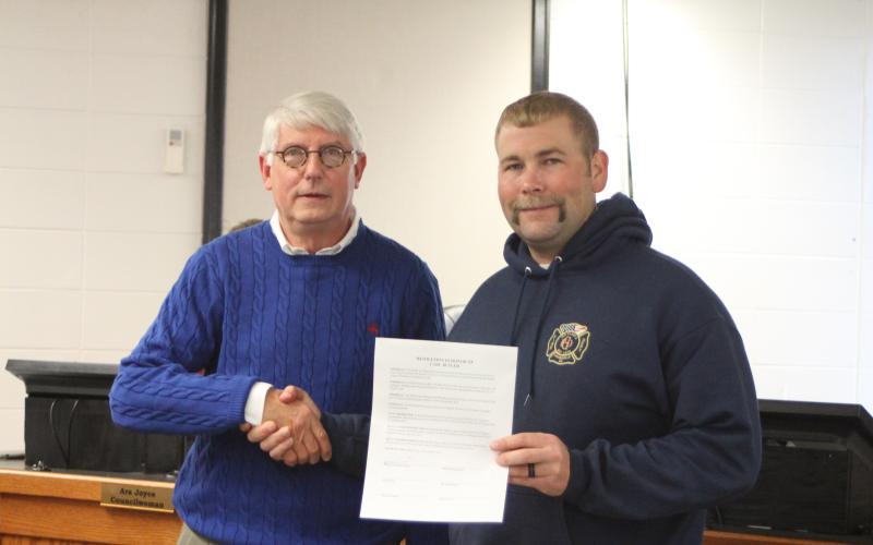 Megan Broome/The Clayton Tribune. Clayton Mayor Jordan Green and Clayton city council members signed a resolution to proclaim that whatever day on which the city of Clayton Christmas parade takes place is hereby declared “Carl Butler Day.” Butler, left, shakes hands with Jordan Green after the city adopted the resolution at Tuesday’s council meeting.