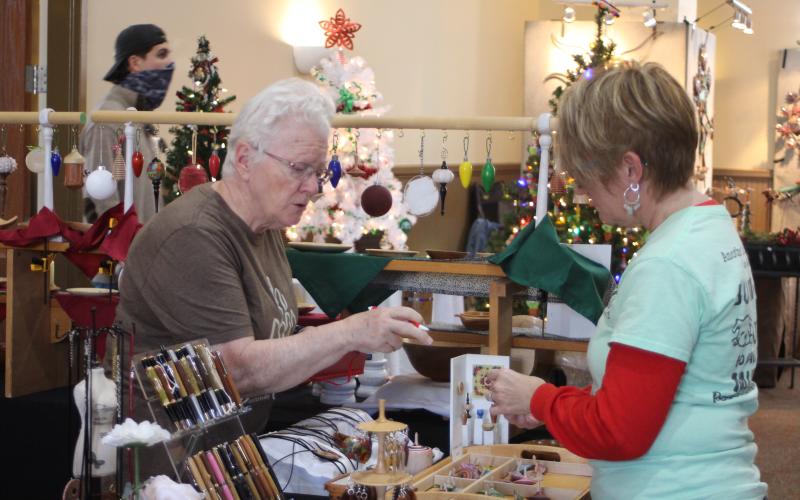 Megan Broome/The Clayton Tribune Booth vendor Joy Moss, left, shows Mary Baer different creations made by John and Joy Moss Woodturners at the Merry Market in the Civic Center last weekend.