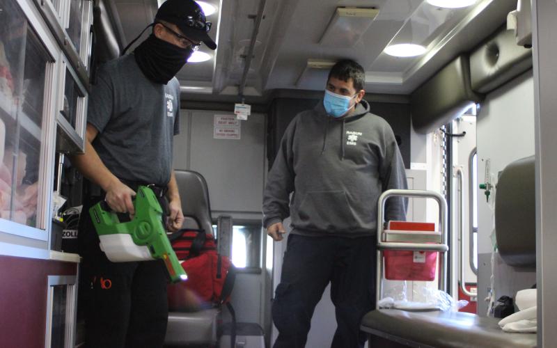 Megan Broome/The Clayton Tribune. Rabun County EMS Paramedics David Jones, left, and Jon Wilbanks decontaminate the back of an ambulance with a spray disinfectant at Station 1 before responding to a call. All ambulances and equipment are brought to the station to be decontaminated after every call as part of safety measures during an uptick in coronavirus cases in the county.