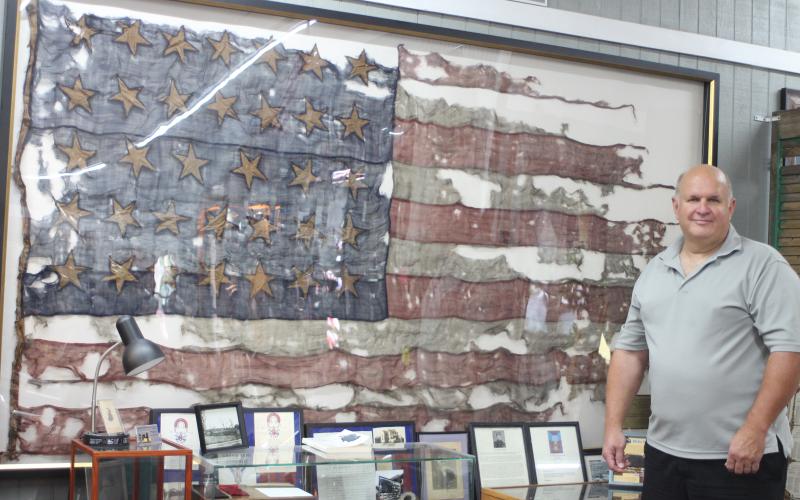 Megan Broome/The Clayton Tribune. Bob Matis, owner of Civil War Corner Antiques in Dillard, owns a United States flag used in the Civil War in the Battle of Cold Harbor on June 3, 1864. It is displayed in his shop along with a display. The flag has 34 stars and two stripes are missing after being torn off in battle.