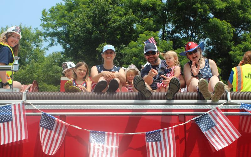 Megan Broome/The Clayton Tribune. Evelyn Gygax, left, Tamsin Gygax, Nola Gygax, Laureanne Gygax, Bob Gygax, Ruby Gygax, and Jordan Vaughn sport their patriotic pride in red, white and blue and ride around Sky Valley on top of a Sky Valley-Scaly Mountain Fire Department truck as part of the city’s Independence Day activities on Saturday.
