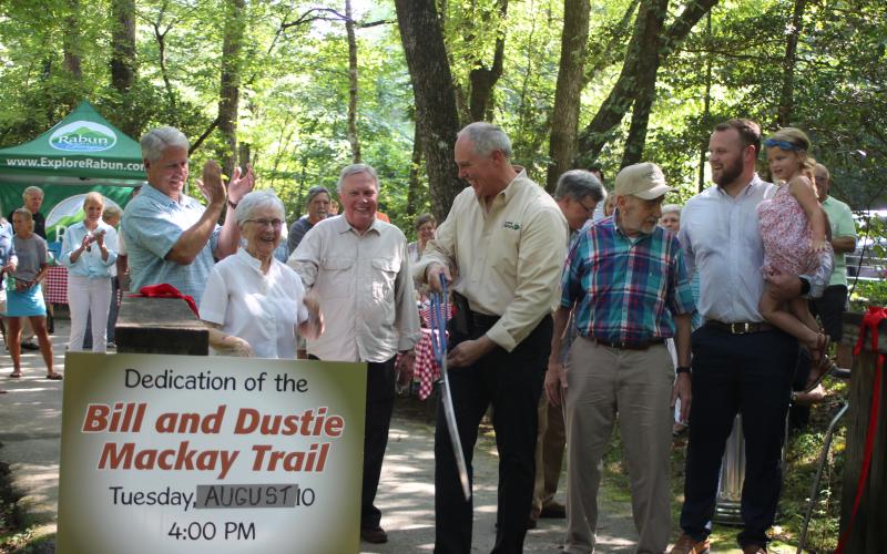 Megan Broome/The Clayton Tribune. The North Entrance to the Tallulah Falls Shortline Trail was dedicated to Bill and Dustie Mackay, who have maintained the trail for 25 years, at a ceremony on Tuesday. Community members, officials and state representatives cut the ribbon: Rep. Stan Gunter, left, Dustie Mackay, Wallace Bruce, Rick Story, director of development for Rabun County, Bill Mackay and State Sen. Bo Hatchett with daughter Hallie.