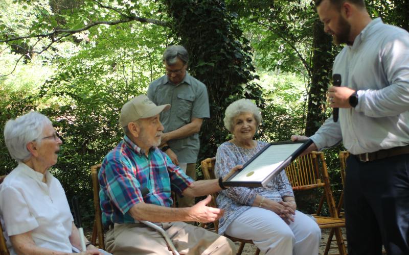 Megan Broome/The Clayton Tribune. Senator Bo Hatchett, right, hands Dustie and Bill Mackay a framed copy of the legislation dedicating the north entrance of the Tallulah Falls Shortline Trail to them. The couple marinated the trail for 25 years.