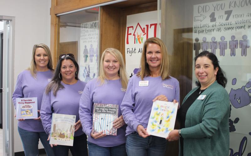 Megan Broome/The Clayton Tribune.  Brooke Cannon, grant administrator, left, Laura Davis, Empowering Families coordinator, Kayla Talley, FAITH legal advocate, Monica Blalock, director of community awareness, present books to Dyana Costello Banks, library manager, for donation to the Rabun County Public Library, in front of the library display.