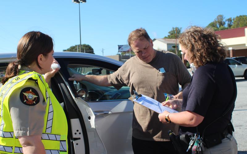 Megan Broome/The Clayton Tribune. Deputy Ana Contreras and Lisa Thompson, coordinator for Safe Kids Rabun County, educate Chris Shelton about car seat safety at a car seat safety inspection checkpoint at the Faith and Blue event last Saturday.