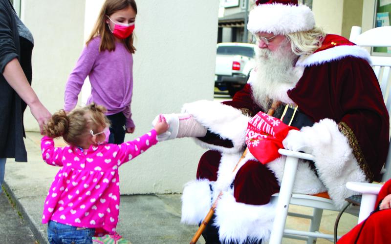 Megan Broome/The Clayton Tribune. Santa hands Lyndi Cox, 2, a candy cane at the Better Homes and Gardens Real Estate company in Clayton last Friday. Winni Cox, 8, is pictured in the background.