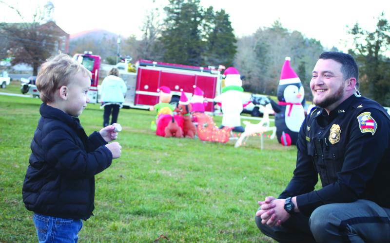 Megan Broome/The Clayton Tribune. Jaxon Golden, left, laughs and talks with Dillard Police Chief Jeremy Parker while eating a S’More at the “A Night Out in Christmastown” event held in Dillard Dec. 8.