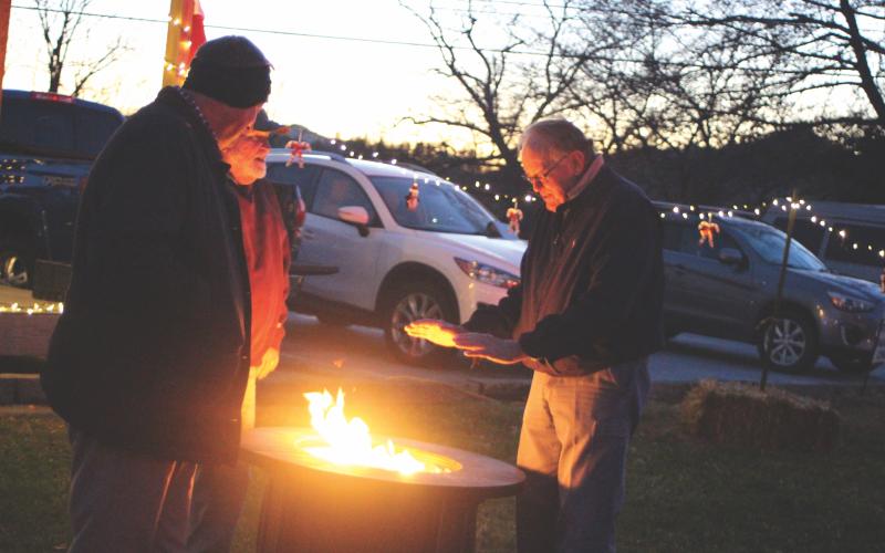 Megan Broome/The Clayton Tribune. Dillard City Council Member Claude Dillard, left, Ron Sanders, and Roy Defoor stay warm around a fire while enjoying caroling and Christmas lights at the  “A Night Out in Christmastown” event held in Dillard Dec. 8.