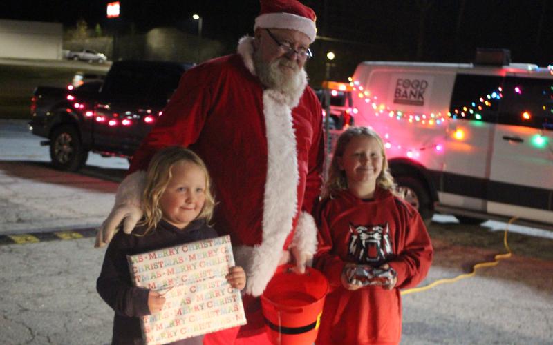 Megan Broome/The Clayton Tribune. Adalyn Moon, 6, and Kiley Moon, 8, talk with Santa and receive gifts at the Christmas toy drive held at the Food Bank of Northeast Georgia last Friday.