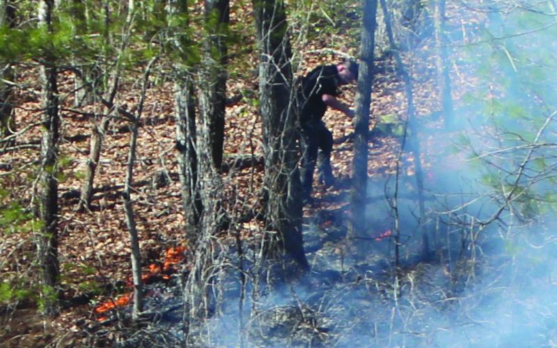 Megan Broome/The Clayton Tribune. Dillard Police Chief Jeremy Parker works to help put out part of the fire on the embankment that spread for acres along the mountains on the north side of Highway 246 in Sky Valley.