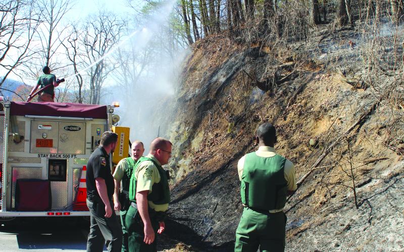 Megan Broome/The Clayton Tribune. USFS Law Enforcement personnel and Dillard Police Department Chief Jeremy Parker analyze the scene of a brush fire that spread along the mountains on the north side of Highway 246 in Sky Valley on the afternoon of March 4. Local firefighters also work to battle the blaze.