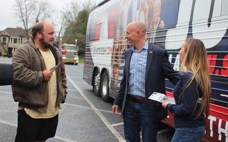 Megan Broome/The Clayton Tribune. U.S. Senate Candidate Josh Clark, center, and Chelsey Clark greet local Justin Stewart at a meet-and-greet at the Clarks’ “Liberty Bus” in Rabun County March 18.