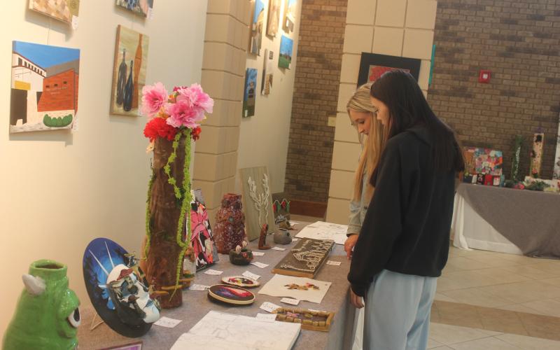 Megan Broome/The Clayton Tribune. Ninth grader Madilyn Gipson and Senior Jade Griffin browse the RCHS Student Art Show held in the Fine Arts Building May 13. Both students had artwork displayed in the show.