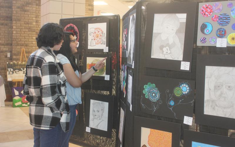 Megan Broome/The Clayton Tribune. Eleventh graders Victoria Merino and Joselyn Gaspar browse the RCHS Student Art Show held in the Fine Arts Building May 13. The show featured artwork from students in grades 9-12.