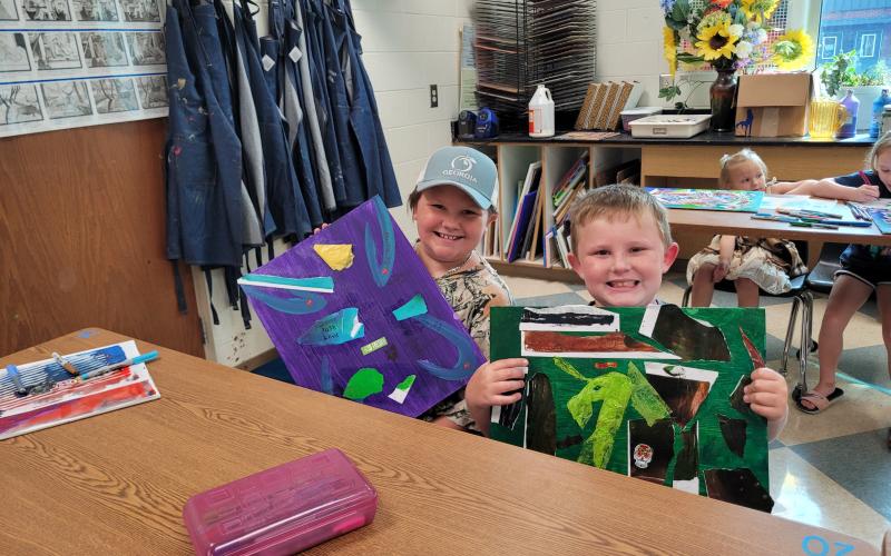 Megan Broome/The Clayton Tribune. Emberlynn Mathis, 10, and Johnathan Thompson, 7, smile from ear to ear and giggle as they showcase their art projects for Mrs. Jarrard’s Art Camp last week. Art camp was held several days last week in the Fine Arts Building at Rabun County High School.