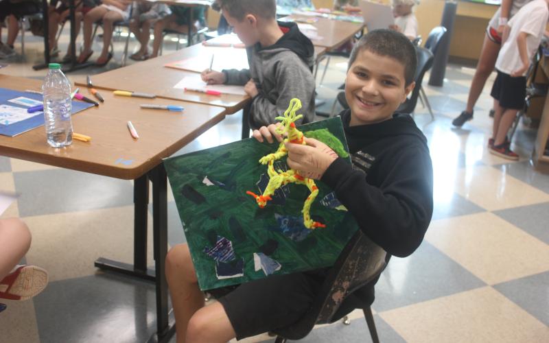 Megan Broome/The Clayton Tribune. Talon Stewart, 10, had his artwork come alive with this dinosaur and painting he created during Mrs. Jarrard’s Art Camp held at the Rabun County High School Fine Arts Building last week.