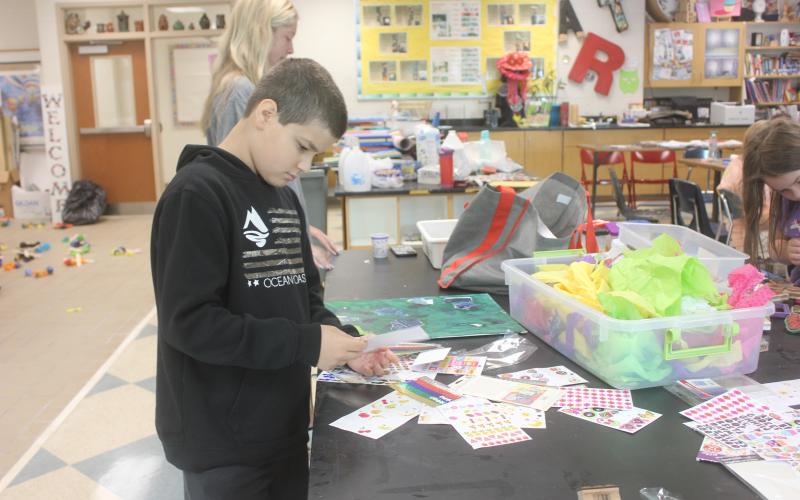 Megan Broome/The Clayton Tribune. Talon Stewart, 10, chooses stickers to complete his masterpiece as he shows off his creativity during Mrs. Jarrard’s Art Camp in the Fine Arts Building at Rabun County High School last week.