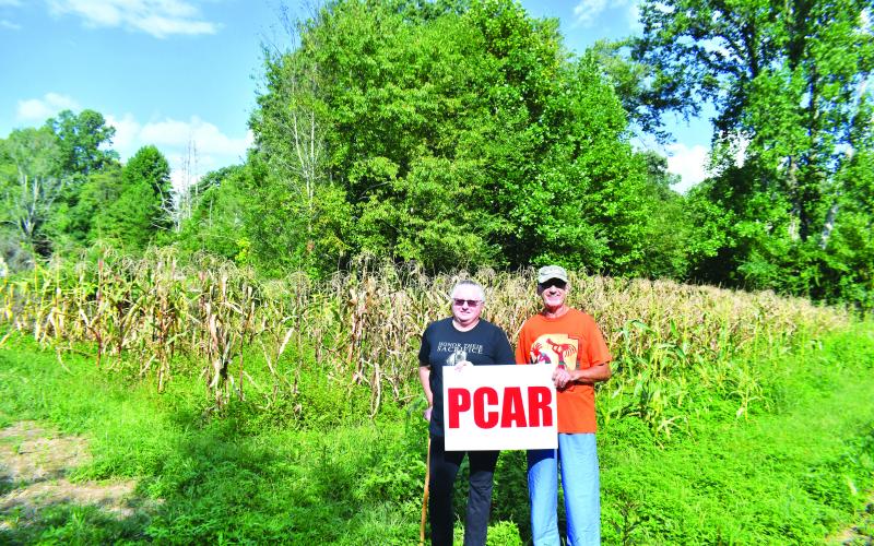 Megan Broome/The Clayton Tribune. Pam Wheeler, CFO of Creating Ties That Bind: For Soldiers and Families Wounded By Loss (left) and Dr. Guy Gober hold a sign representing the Nonprofit Prostate Cancer Awareness Resources, Inc. (PCAR). Both nonprofits are hosting the Inaugural Tiger Corn Festival Sept. 24 and members of the public will be able to purchase ears of organic corn from this field during the festival.