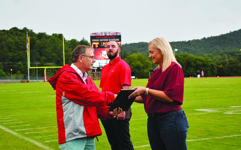 Enoch Autry/The Clayton Tribune. Rabun County Hall of Fame committee member Tom Law presents Tricia Taylor, a state champion in the shot put competition in the late 1980s her honor. In the background is Tanner Plemmons, a shooting guard for the Rabun County High basketball Wildcats who was named all-state three straight years from 2010 through 2012.