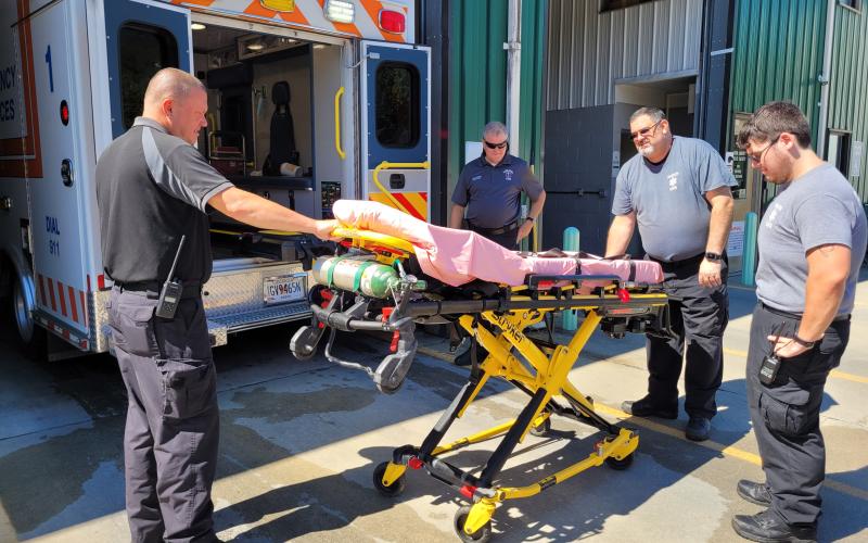 Megan Broome/The Clayton Tribune. Rabun County EMS Captain Trampes Stancil, EMS/911 Director Mike Carnes; Paramedic Don White and EMT Will Shanks demonstrate how the Stryker Power Load System automatic hydraulic lifting equipment lifts patients who are on stretchers in and out of the ambulance. This system significantly helps reduce workplace injuries.