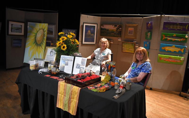 Megan Broome/The Clayton Tribune. Tricia Moore, festival chairman, and Tanya Barton work the booth featuring a tribute and memoriam to Lee Johnson, a well known Clayton artist and long time member of the guild.