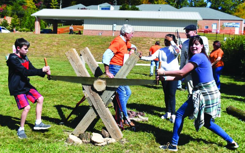 Megan Broome/The Clayton Tribune. Jacoby Ellison and Amber Boyd participate in the log-sawing activity at the Foxfire Mountaineer Festival. Also pictured is volunteer Ted Altholz keeping the piece steady as they saw the log. Vladimir Kasperovich and Gabriella Pillay look on during the activity.