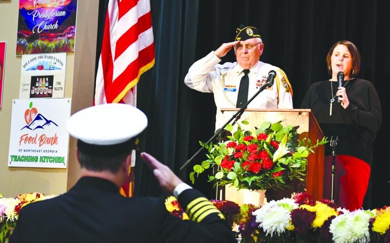 Megan Broome/The Clayton Tribune. Veteran Doug Wayne and fellow soldiers salute the American Flag as Lora Burrell sings The Star-Spangled Banner at the opening of the Veterans Appreciation Dinner held at the Rabun County Civic Center.
